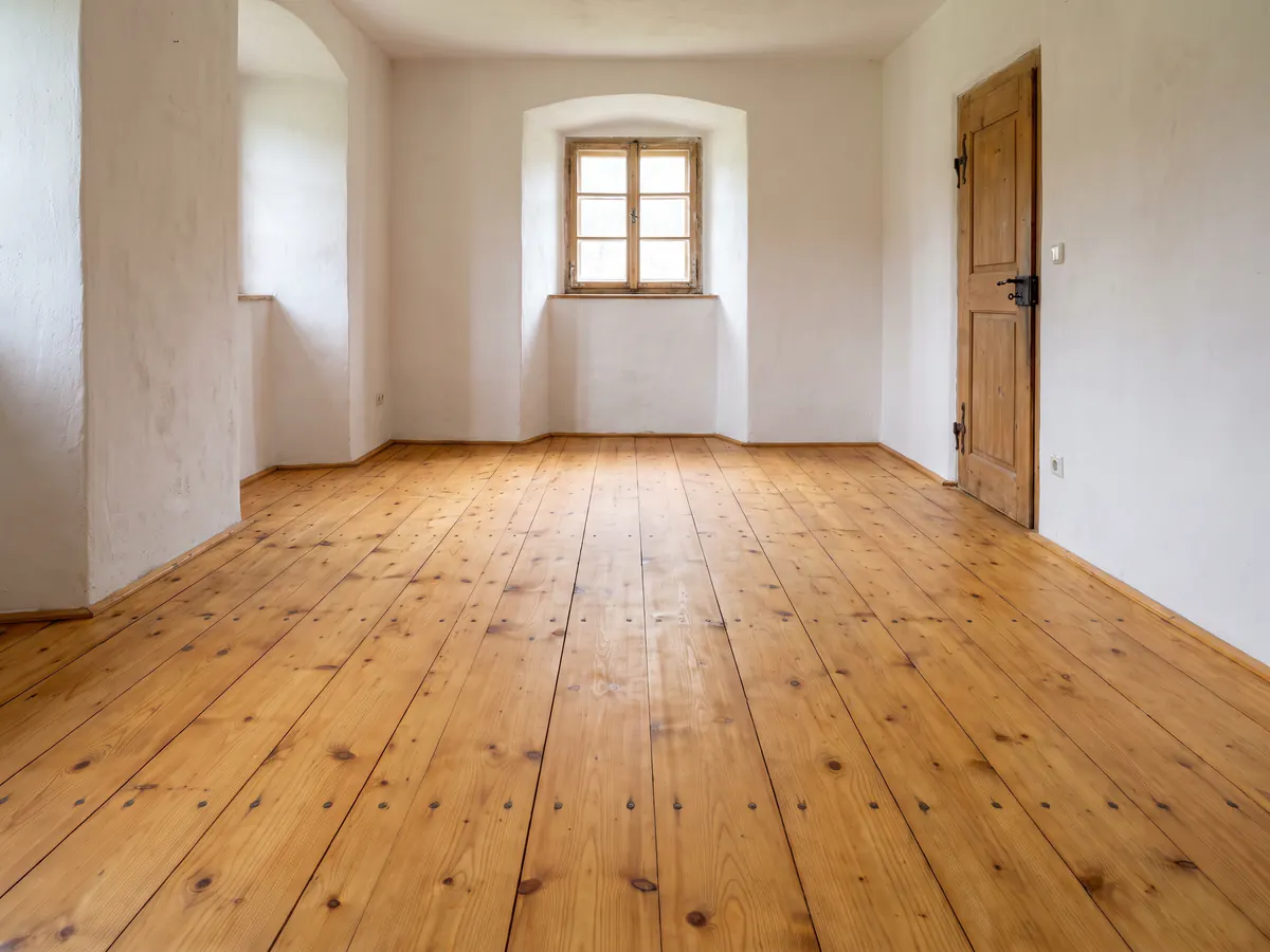 Dasselbe Landhauszimmer mit frisch geschliffenen und geölten breiten Dielen in warmem Honigton, Äste und Nagelköpfe sichtbar
